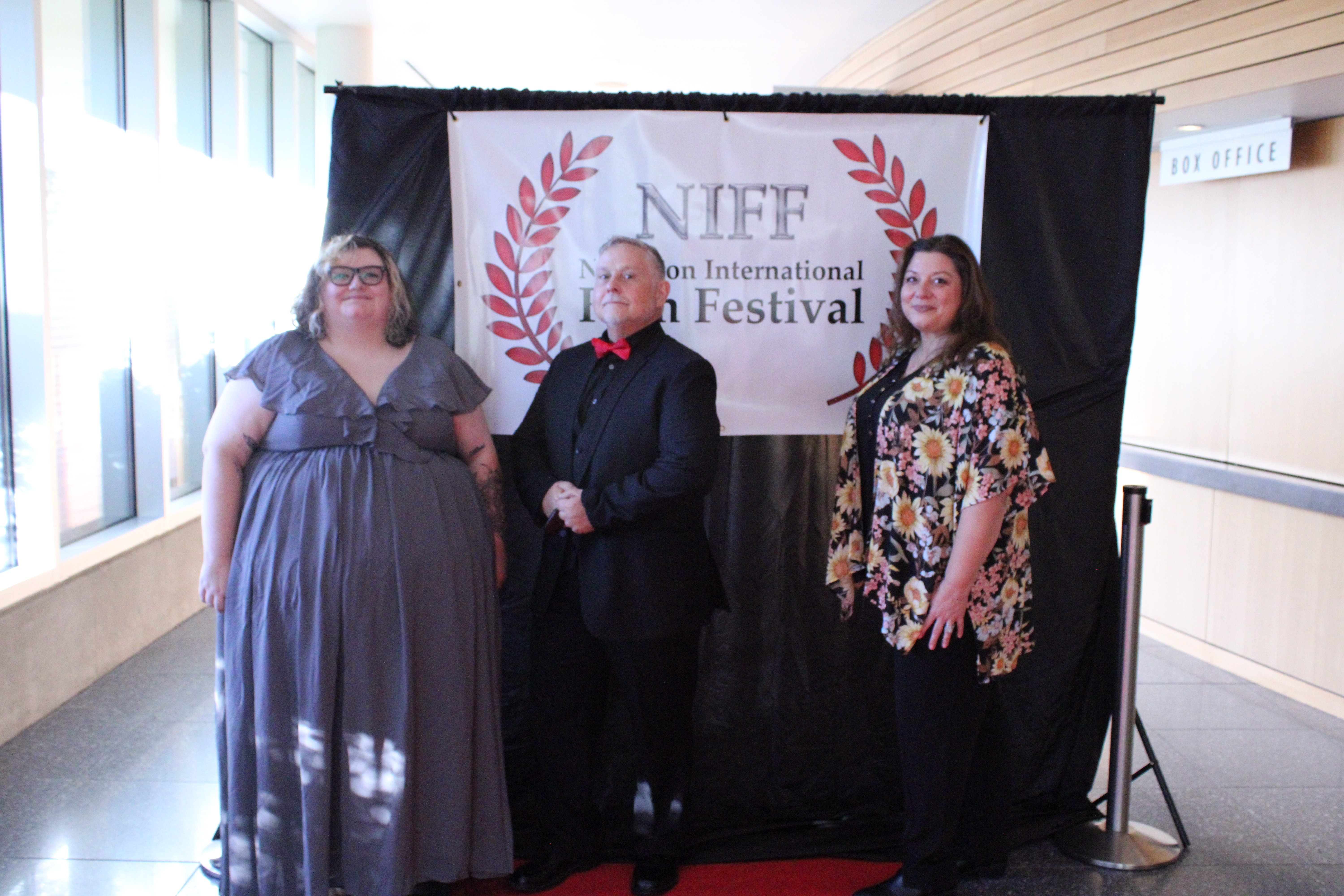 three members of the Rotaract club posing for a group image in front of the NIFF backdrop.