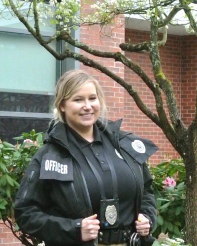 Summer Comte headshot taken outdoors on-campus. Wearing safety officer uniform and badge